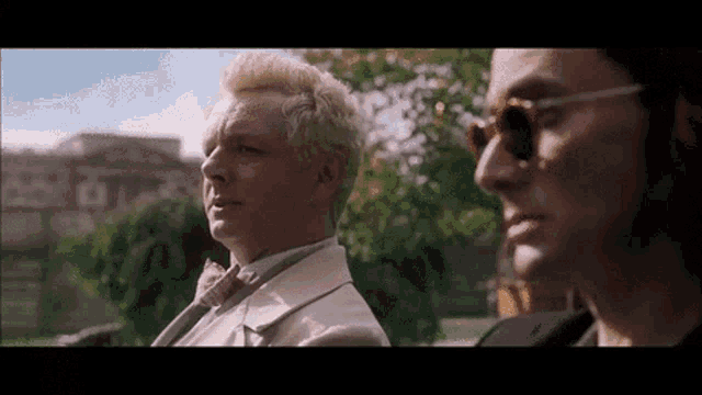 two men in suits and bow ties are standing next to each other in a park .