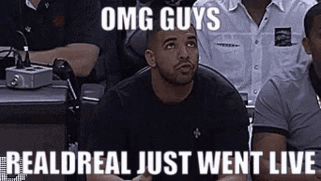 a man is sitting in the stands at a basketball game with a meme that says omg guys realdreal just went live