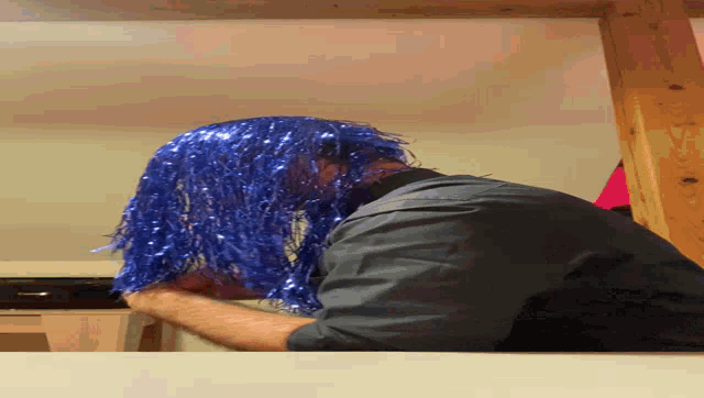 a man wearing a blue tinsel wig is laying on his back