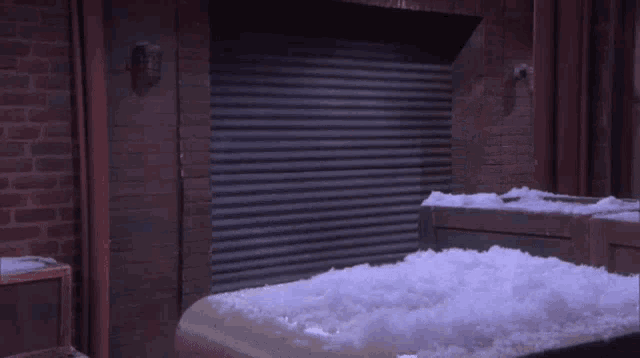 a woman is standing in front of a brick building in the snow looking at her phone .
