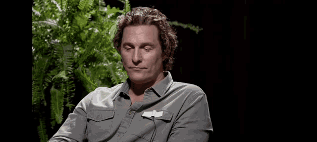 a man in a gray shirt is sitting in front of a plant and looking down .