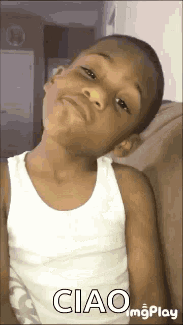 a young boy wearing a white tank top is making a funny face and says ciao .