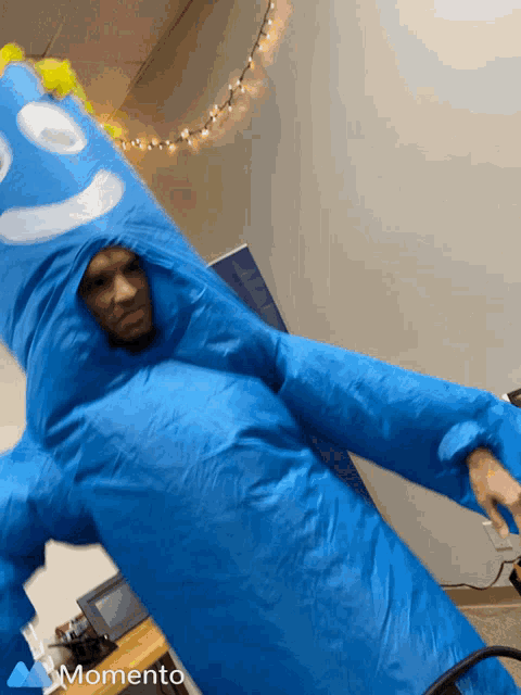 a man in a blue inflatable monster costume with the word momento on the bottom right
