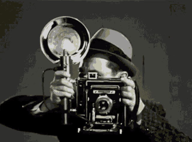 a man in a fedora is taking a picture with a camera that says ' oi ' on it
