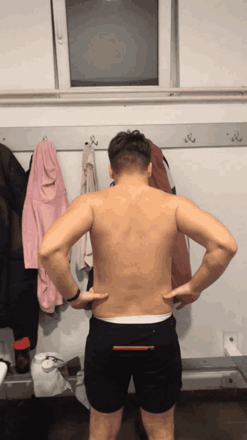 a shirtless man stands in a locker room with his hands on his back