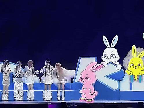a group of people standing on a stage with a pink bunny in the middle