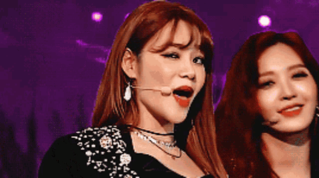 a woman with red hair is singing into a microphone while standing next to another woman