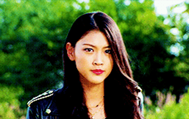a woman in a black leather jacket is standing in front of trees .