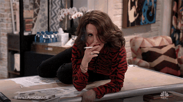 a woman is laying on a table with a cigarette in her mouth and the hashtag #willandgrace