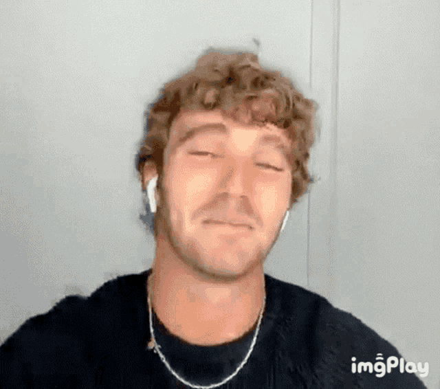 a man with curly hair wearing headphones and a necklace is making a funny face .