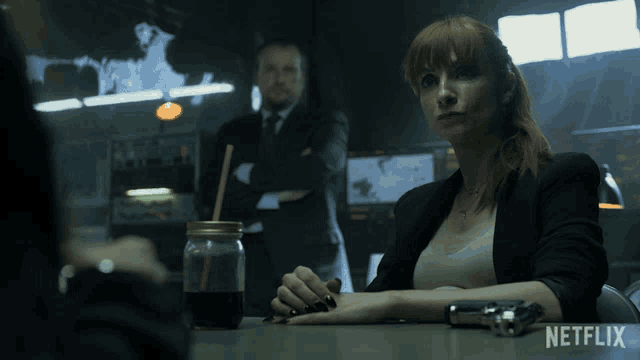 a woman sits at a table with a gun and a netflix logo in the corner