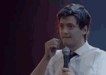 a man in a white shirt and tie is holding a microphone and making a funny face .