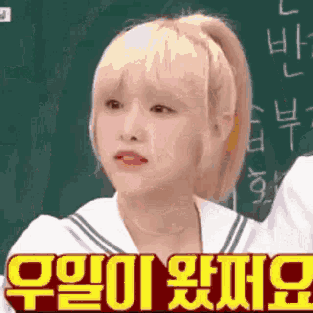 a girl in a sailor suit is standing in front of a blackboard and making a funny face .