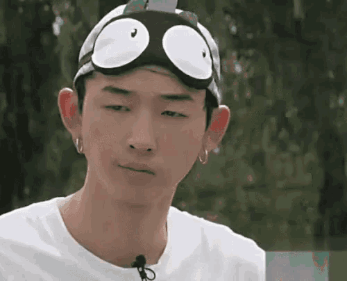 a young man wearing a hat with googly eyes and goggles is making a funny face .