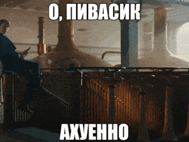 a man in a suit sits on a railing in front of a brewery with russian writing