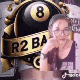 a woman wearing glasses is sitting in front of a pool table with a pool ball in the background .