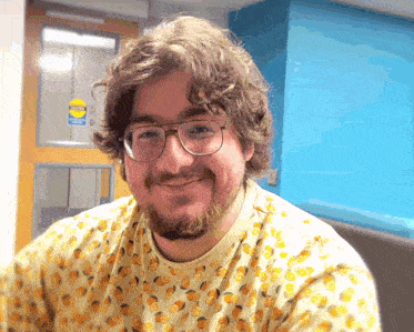 a man wearing glasses and a shirt with oranges on it smiles in front of a door that has a caution sign on it