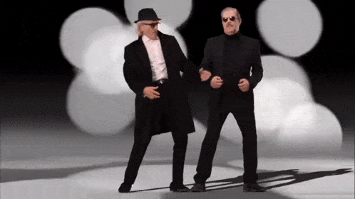 two men in suits and hats are dancing together in a dark room