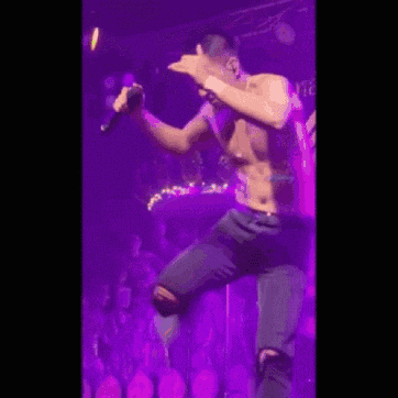 a shirtless man is holding a microphone on a stage .