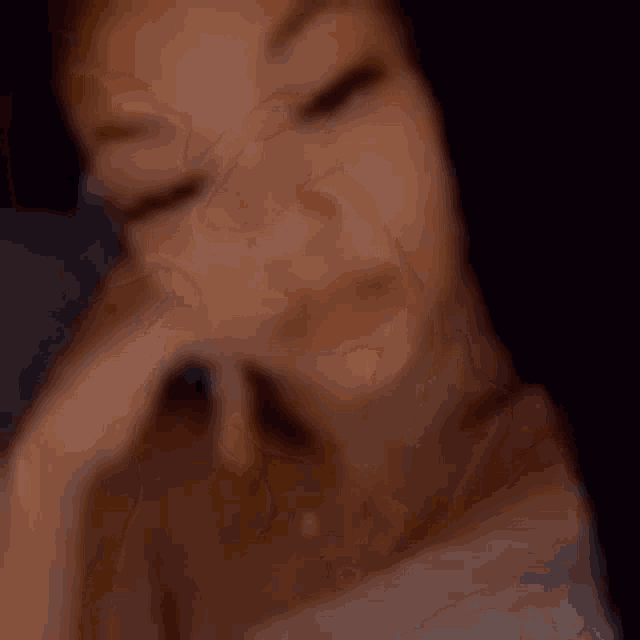 a blurry picture of a woman with her hand on her face .