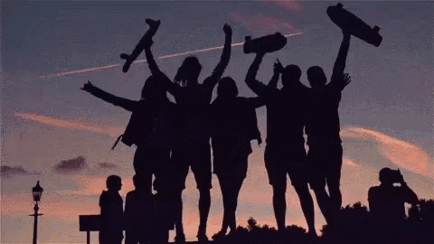 a group of people holding their skateboards in the air at sunset