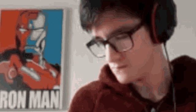 a man wearing headphones and glasses is looking at a poster of iron man .