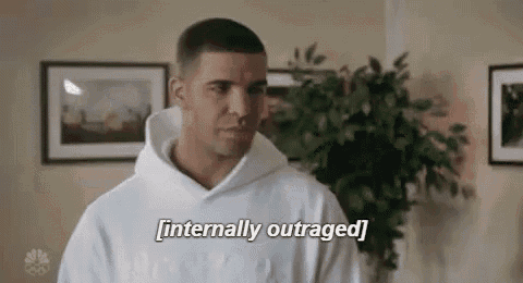 a man in a white hoodie is saying `` internally outraged '' while standing in a living room .