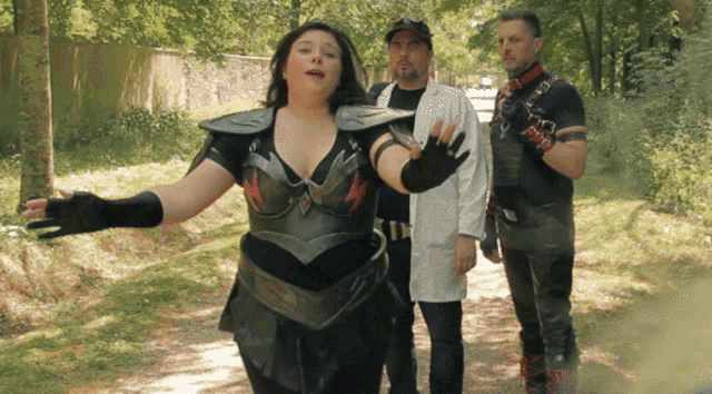 a woman in armor stands between two men in costume