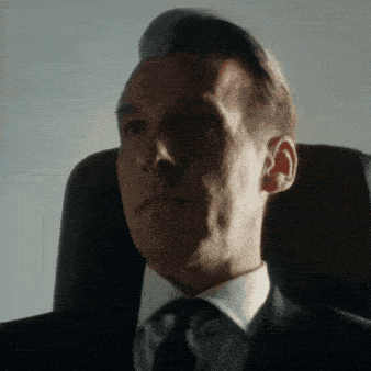 a man in a suit and tie is sitting in a dark chair