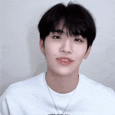 a young man wearing a white shirt and a necklace with the letter t on it