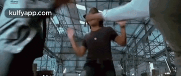 a man in a black shirt is being punched in the face by a woman in a warehouse .