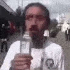 a man with a beard is holding a microphone in his hand and talking into it .