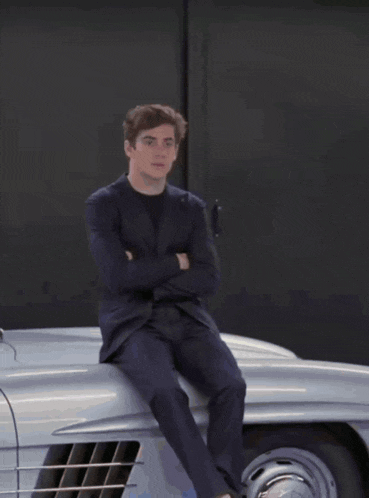 a man in a suit sits on the hood of a car