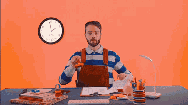 a man sits at a desk in front of a clock that shows the time as almost 3:00