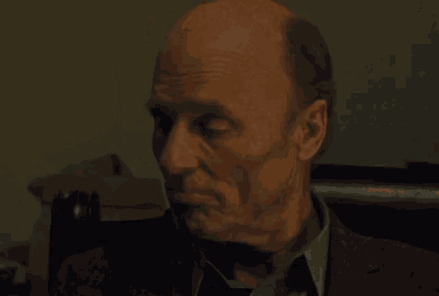 a bald man in a suit and tie is sitting in a chair .