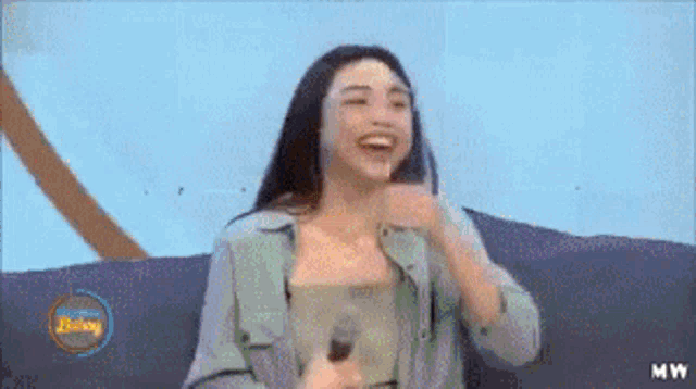 a woman is sitting on a couch with a microphone and laughing .