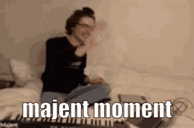 a person is sitting on a bed with a laptop and a keyboard and the words majent moment .