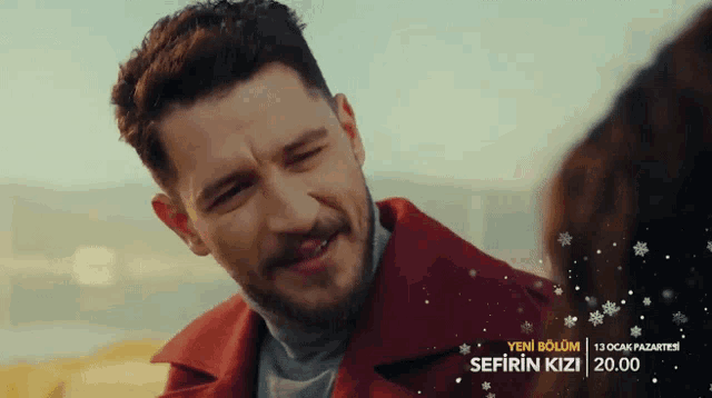 a man in a red coat is smiling in front of a sign that says yeni bolum sefirin kizi 20.00