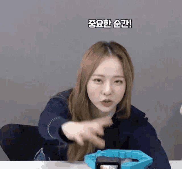 a young woman is sitting at a table with a blue toy in front of her and pointing at it .