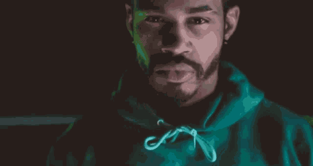 a man with a beard is wearing a green hoodie and looking at the camera