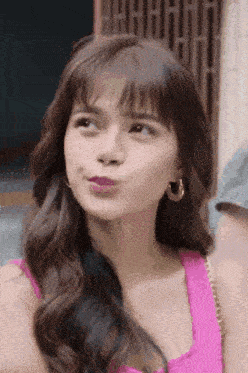 a woman wearing a pink tank top and hoop earrings is making a funny face