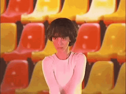 a woman is standing in front of a row of red and yellow chairs in a stadium .