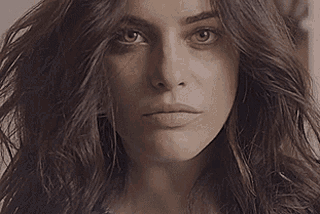 a woman with long brown hair is looking at the camera