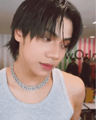 a close up of a person wearing a necklace and a grey tank top