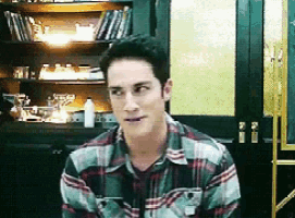 a man in a plaid shirt is sitting in front of a bookcase