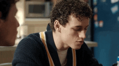 a young man with curly hair is sitting at a table with another young man .