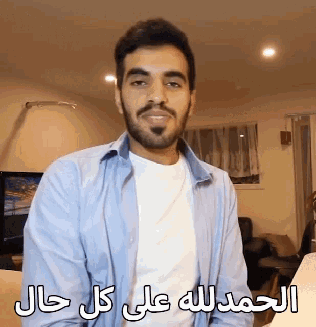 a man with a beard is wearing a blue shirt and a white t-shirt with arabic writing on it