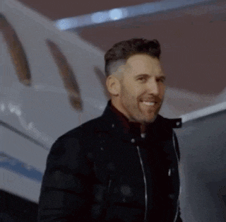 a man in a black jacket is smiling while standing in front of a plane .
