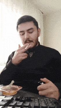a man is smoking a cigarette while sitting at a keyboard