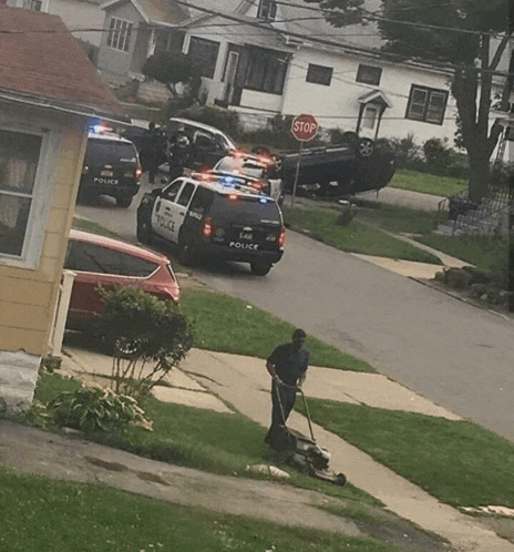 a man mowing the grass in front of a police car